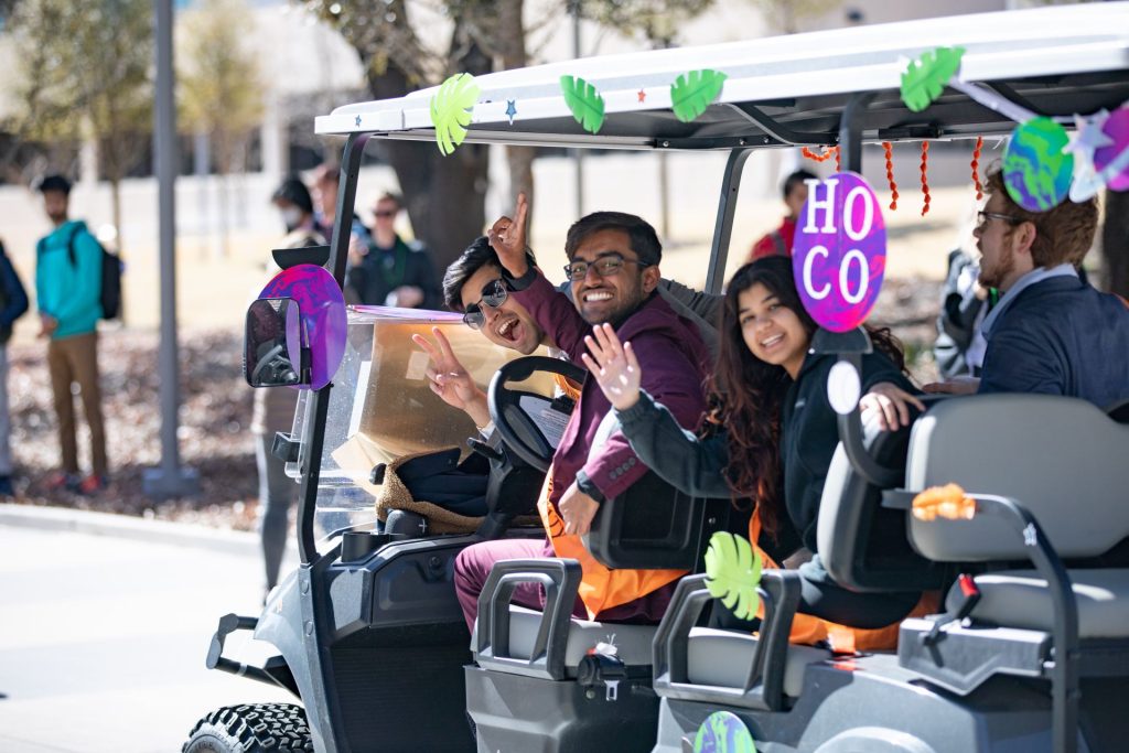 Students riding a golf cart waving.