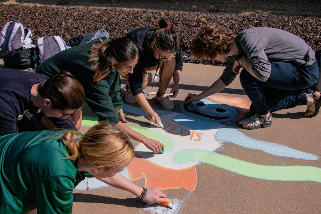 Students drawing UT Dallas mascot Temoc on the sidewalk with chalk.