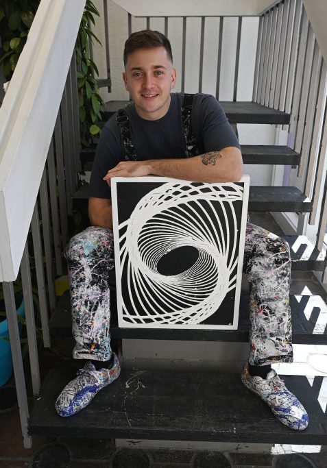 Cole Newman sitting on stairs holding a black and white painting he created.