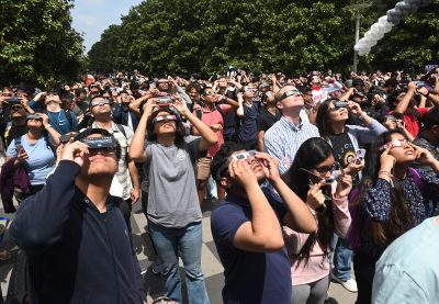 Crowd of people wearing solar eclipse glasses while looking up at the sun.