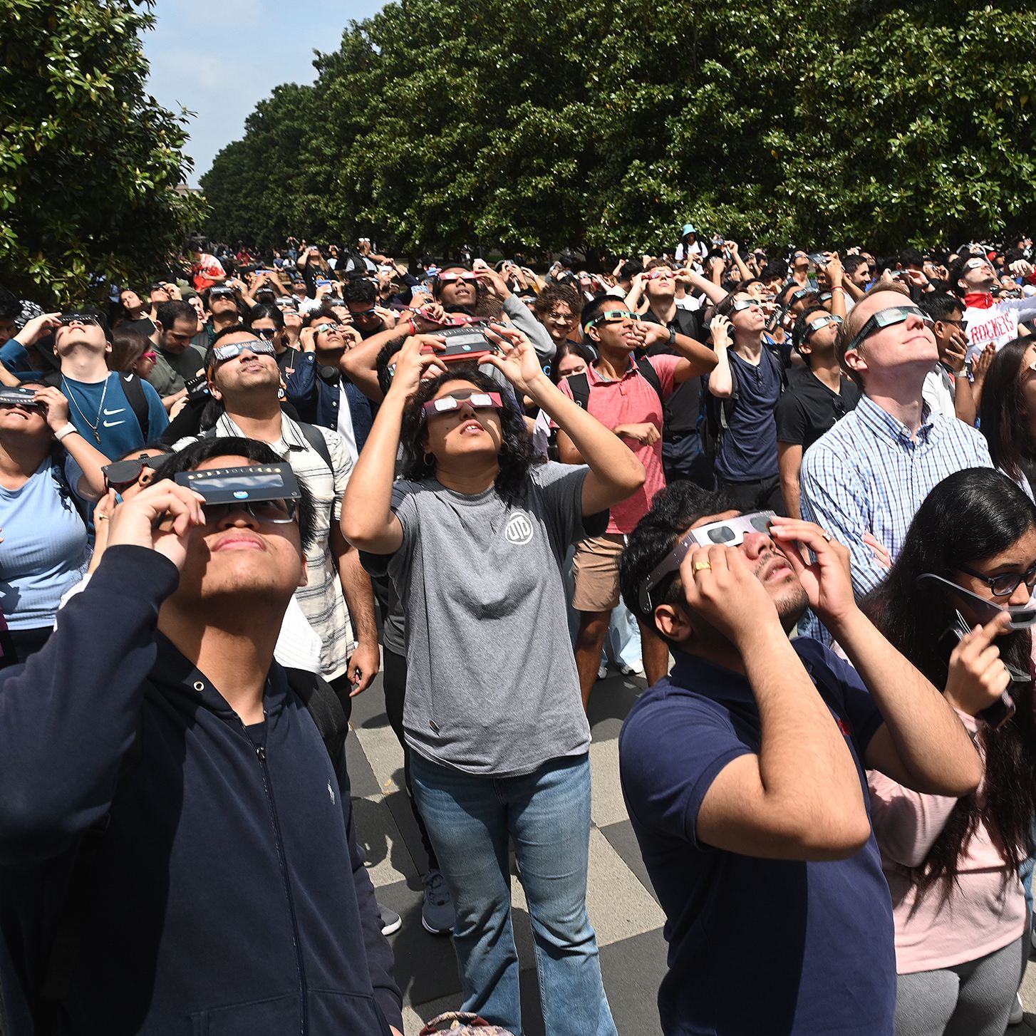 Photo Gallery: Eclipse Brings Campus Community Outside for a Glimpse. Group of people wearing eclipse glasses while looking up at the sun.