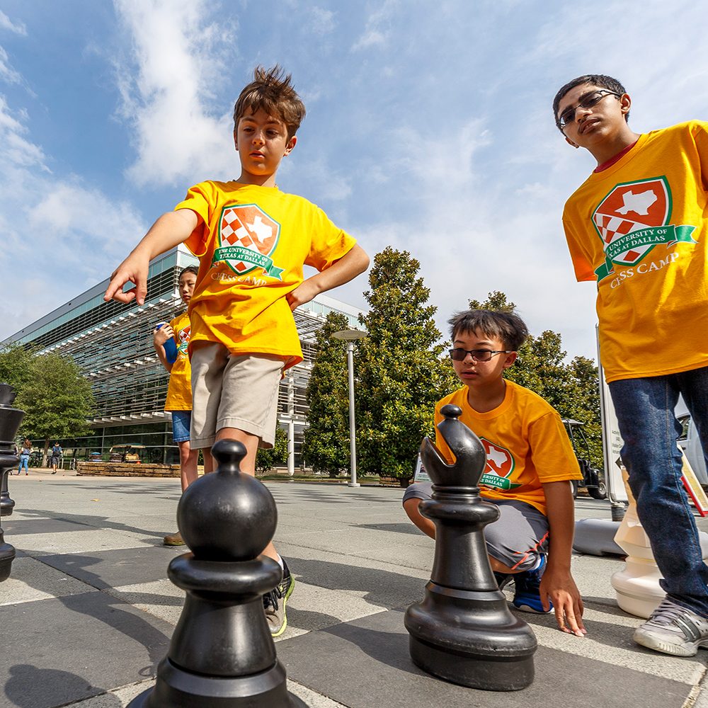 UT Dallas Magazine. Children play a game of chess with giant pieces on an outdoor chessboard on the campus of The University of Texas at Dallas.